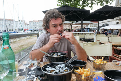 Young man eating mussels on a terrace of a french restaurant