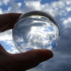 Close-up of hand holding crystal ball against sky