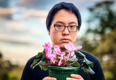 Portrait of young man holding pink flowering cyclamen plant.