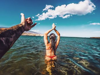 Cropped hand gesturing while woman standing with hands clasped in sea