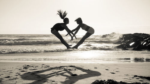 Silhouette of women jumping on beach against clear sky