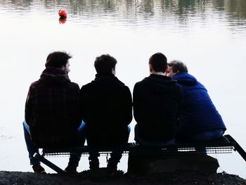 Rear view of men sitting by lake