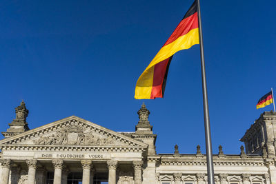 Low angle view of german flag on reichstag building against clear blue sky during sunny day