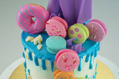 Close-up of multi colored macaroons with donut on cake against gray background