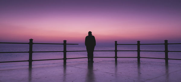Rear view of silhouette man standing on railing against sea