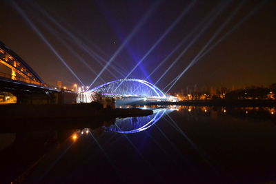 Illuminated bridge over river against sky at night