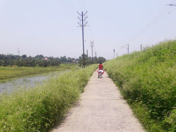 Rear view of woman cycling on road amidst field against sky