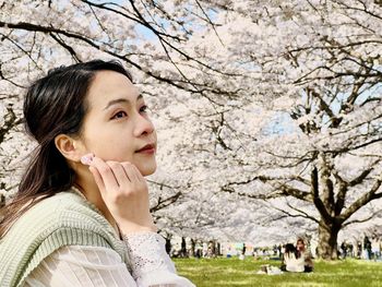 Portrait of young woman standing against cherry blossom