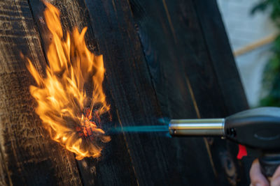 Cropped hand holding blow torch against wood