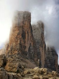 Low angle view of rocks on mountain against cloudy sky