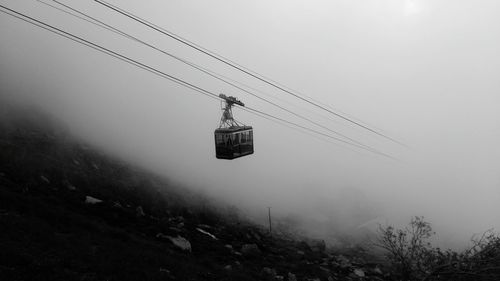 Low angle view of overhead cable car against sky during foggy weather