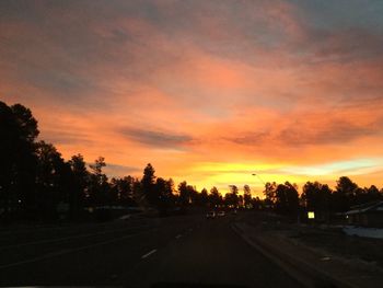 Road by silhouette trees against dramatic sky during sunset