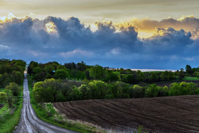 Panoramic shot of road amidst field against sky during sunset