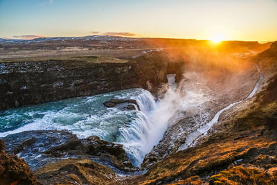 Scenic view of waterfall against sky during sunset