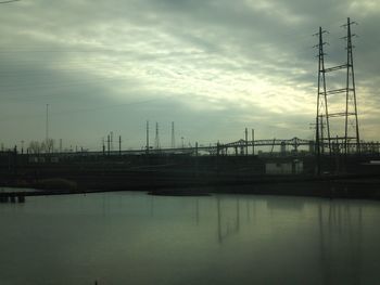 Silhouette electricity pylon by river against sky