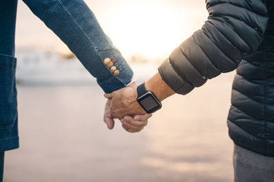 Cropped image of senior woman wearing smart watch while holding man's hand at harbor