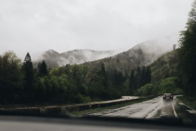 Road amidst trees and mountains against sky