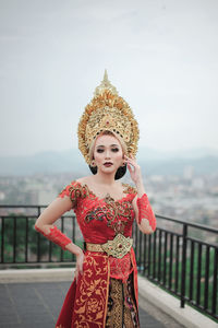 Woman with custome traditional of bali  standing by railing against clear sky