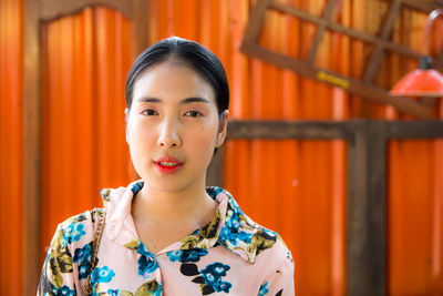 Portrait of young woman standing against orange wall