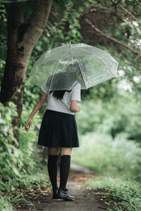 Rear view of woman with umbrella standing in rain