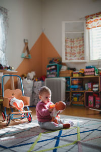 A baby girl sitting on carpet playing with her dolls