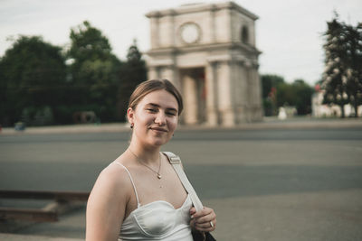 Portrait of young woman standing against building