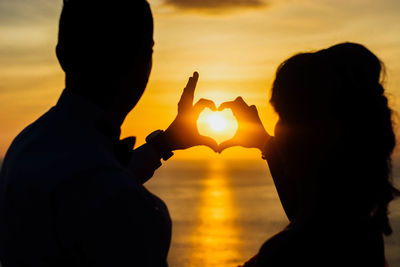 Close-up of silhouette couple making heart shape against sky during sunset