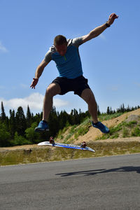 Low section of man jumping on road against sky