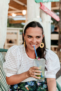 Portrait of happy and smiling young woman in stylish summer clothes drinking cocktail in bar.