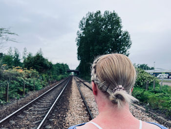 Rear view of woman standing on railroad track against sky