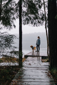 Full length of woman with dog standing on pier by lake