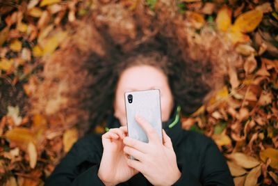 Directly above shot of woman using phone while lying on field at park