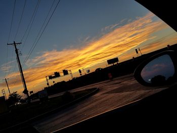 Power lines against cloudy sky at sunset