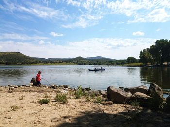 Man sitting on riverbank against sky