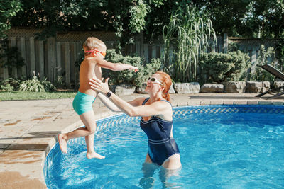 Caucasian mother training toddler son to swim in swimming pool outdoor. baby boy diving 