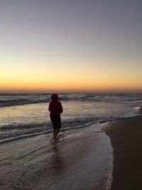 Rear view of silhouette man walking on beach against sky during sunset