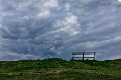 Empty park bench on hill against cloudy sky