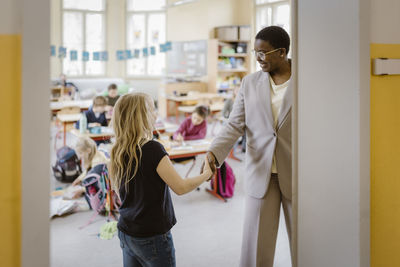 Smiling female teacher doing handshake with schoolgirl in classroom