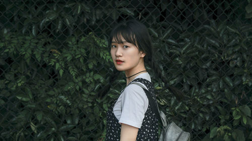 Portrait of beautiful young woman standing against plants