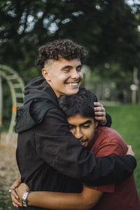 Happy boy embracing teenage male friend at park