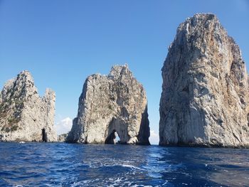 Rock formations in sea against clear blue sky