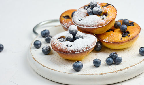 Round mini cottage cheese pies with blueberries on a white wooden board, delicious sweet dessert