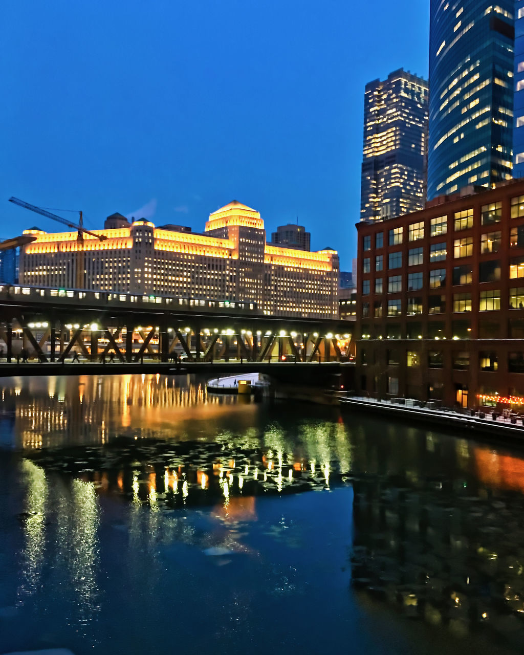 ILLUMINATED CITY AT WATERFRONT AGAINST BLUE SKY