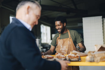 Smiling male baker with customer buying buns at bakery