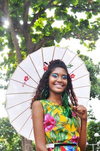 Portrait of young woman with umbrella standing against trees