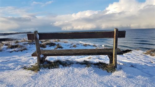 Wooden post on snow covered land by sea against sky