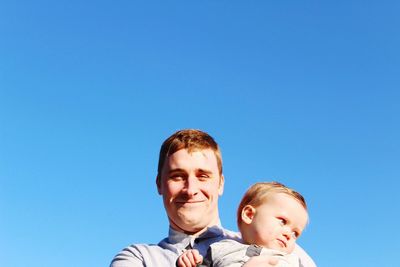 Low angle view of father with toddler against clear blue sky