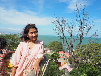 Portrait of smiling young woman standing against sky