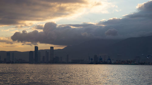 Sea by buildings against sky during sunset