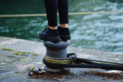 Low section of man standing on bollard at harbor